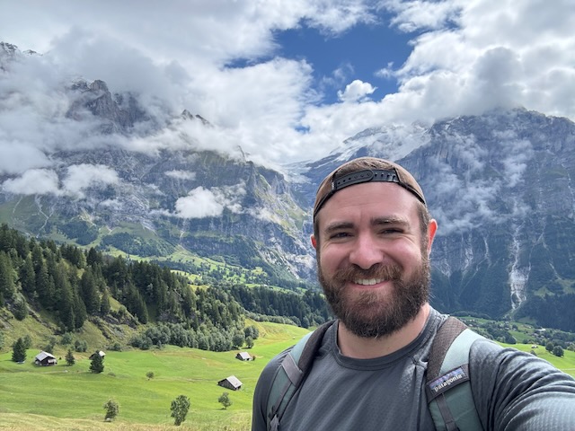 Elliot Milco on a hike in Grindelwald, Switzerland. In the background you can see massive mountains swathed in clouds.